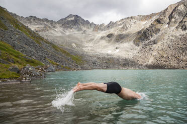 Mann taucht zum Schwimmen in den Upper Reed Lake, Talkeetna Mountains, Alaska - CAVF86649