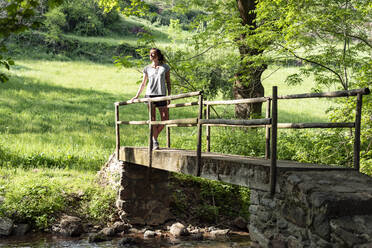 Fitte Frau, die auf einer Holzbrücke steht und in den Wald schaut - CAVF86661