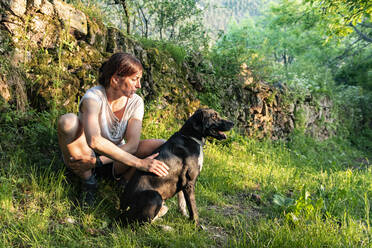 Woman petting and playing with her dog in a forest. - CAVF86664