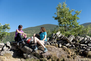 Zwei Wandererinnen ruhen sich auf einem Bergpfad aus und unterhalten sich. - CAVF86668