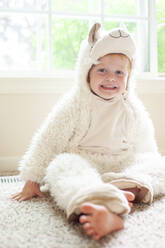 Porträt eines glücklichen kleinen Jungen im Lamakostüm, der zu Hause auf dem Boden sitzt - CAVF86691