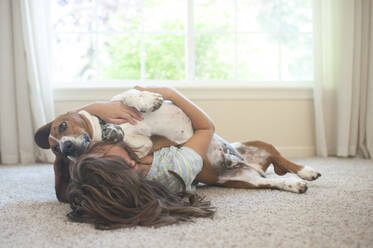 Junges Mädchen liegt mit ihrem Basset Hound zu Hause auf dem Boden - CAVF86692