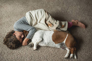 Young girl laying on the floor in blanket with basset hound dog - CAVF86693