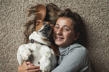 Tween Girl posiert mit ihrem Basset Hound auf dem Teppich liegend - CAVF86695
