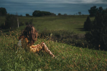 Tween Mädchen schaut weg auf einem grünen Hügel mit dunklem Himmel - CAVF86699