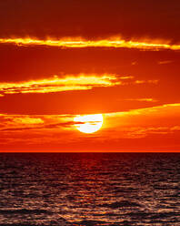 Die Sonne geht am Horizont des Ozeans unter und lässt die Wolken in Flammen aufgehen. - CAVF86753