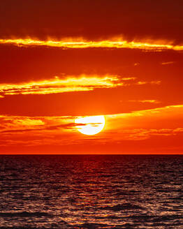 Die Sonne geht am Horizont des Ozeans unter und lässt die Wolken in Flammen aufgehen. - CAVF86753