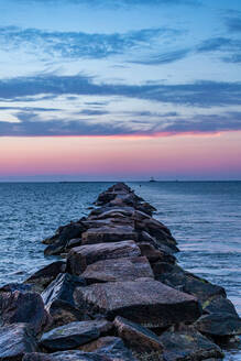 Ein Felsenpier, der unter einem rosafarbenen Sonnenuntergangshimmel ins Meer hinausführt. - CAVF86762