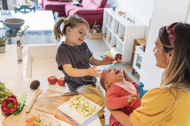 Happy mother and daughter playing with baby girl in kitchen at home - JAF00030