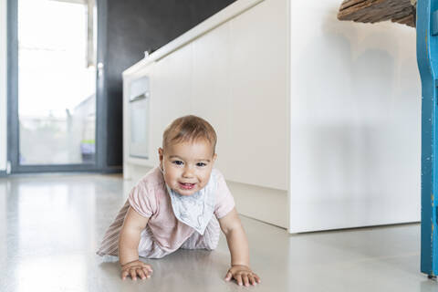 Süßes Baby Mädchen krabbeln auf dem Boden in der modernen Küche zu Hause, lizenzfreies Stockfoto