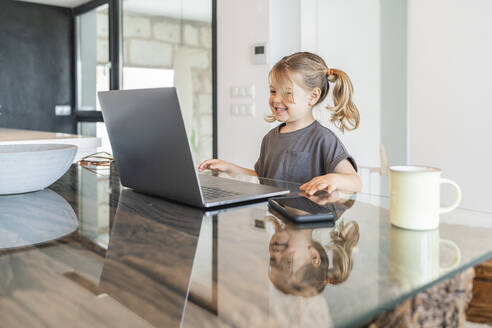Smiling cute girl studying over laptop on table at home - JAF00037