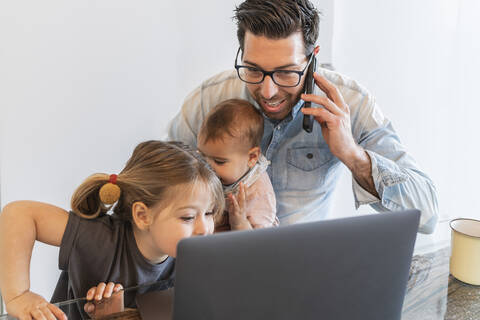 Vater spricht über Smartphone mit seinen Töchtern zu Hause, lizenzfreies Stockfoto