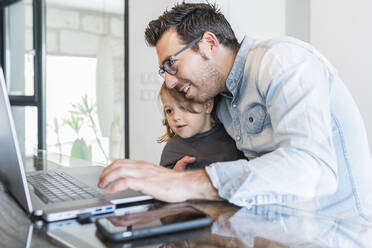 Father embracing daughter while working on laptop at home - JAF00044