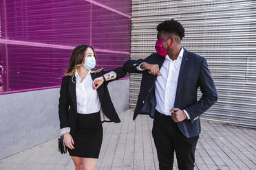 Geschäftsleute, die Masken tragen, stoßen mit dem Ellbogen an, während sie an einem Gebäude in der Stadt stehen - LJF01631