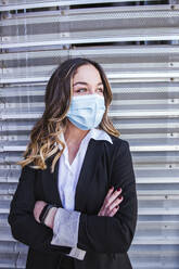 Close-up of businesswoman wearing mask standing against wall in city - LJF01640