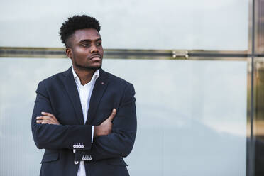 Thoughtful businessman with arms crossed standing against wall in city - LJF01645