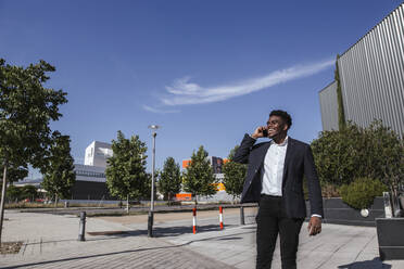 Fröhlicher Geschäftsmann, der über sein Smartphone spricht, während er an einem sonnigen Tag in der Stadt steht - LJF01654