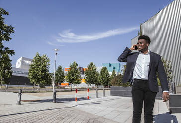 Male professional talking over smart phone while standing in city during sunny day - LJF01655