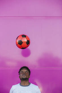 Young man juggling with soccer ball against pink wall in city - LJF01679