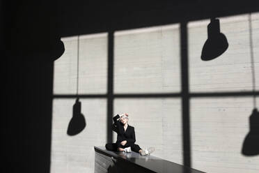 Weiblicher Profi in elegantem Anzug entspannt sich auf einer Stützmauer mit Sonnenlicht und Schatten im Hintergrund - TCEF00813