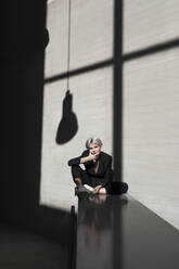 Stilvolle weibliche professionelle tragen Anzug entspannt auf Stützmauer mit Sonnenlicht und Schatten im Hintergrund - TCEF00823