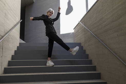 Businesswoman wearing elegant suit dancing on steps in building - TCEF00827