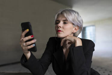Nahaufnahme einer Geschäftsfrau im schwarzen Anzug, die im Büro sitzend ein Smartphone benutzt - TCEF00828