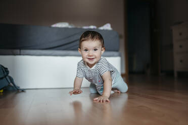 Portrait of smiling baby girl crawling on floor of bedroom - GEMF03893