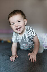 Portrait of happy baby girl crawling on bed - GEMF03894