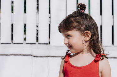 Portrait of little girl wearing red summer dress in front of white wall - GEMF03904