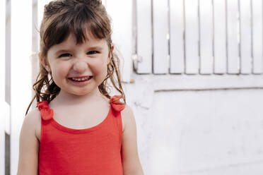 Portrait of little girl wearing red summer dress in front of white wall - GEMF03905