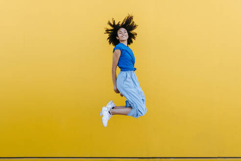 Pretty woman jumping for joy in front of yellow wall - TCEF00842