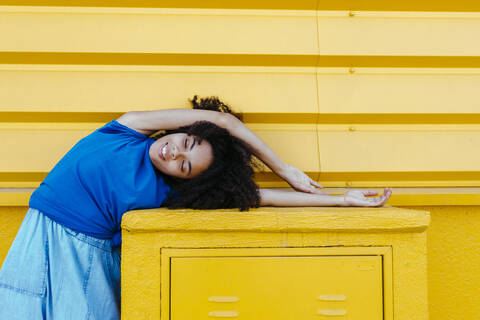 Verträumte Frau beugt sich seitwärts über eine Platte vor einer gelben Wand, lizenzfreies Stockfoto