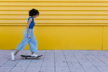 Young woman skateboarding in front of yellow wall - TCEF00856