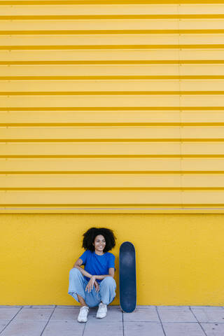 Young woman with skateboard sitting in front of yellow wal stock photo