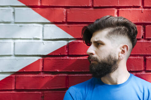 Young man with tattoo standing in front of red brick wall, portrait - EYAF01203