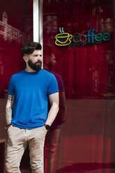 Young man leaning on windowpane of coffee shop - EYAF01209