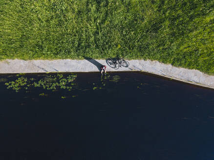 Drohnenaufnahme eines mittelgroßen erwachsenen Mannes mit Fahrrad am Flussufer - KNTF04771