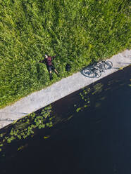 Luftaufnahme eines mittleren erwachsenen Mannes mit Fahrrad auf einer Wiese am Flussufer - KNTF04773