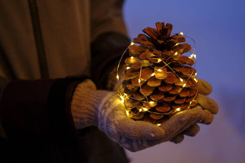 Beleuchteter Tannenzapfen in der Hand eines Mädchens zu Weihnachten - LBF03129