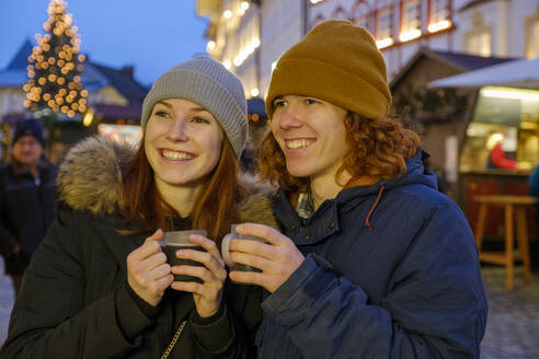Happy young couple holding coffee cups at Christmas market - LBF03130