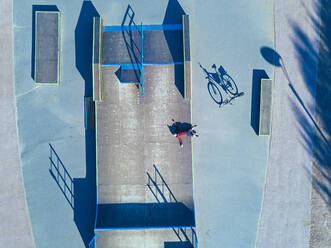 Man lying on concrete ramp in skate park, aerial view - KNTF04778