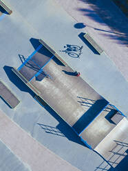 Man sitting on concrete ramp in skate park, aerial view - KNTF04780