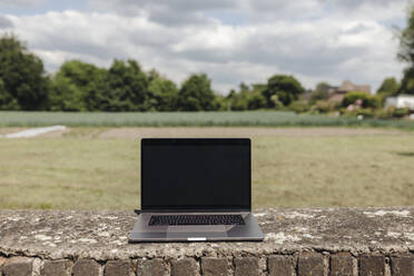 Laptop an einer Backsteinmauer auf dem Lande - GUSF04010