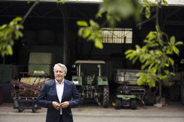 Senior businessman on a farm with tractor in barn - GUSF04025