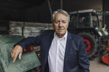 Portrait of a senior businessman on a farm with tractor in barn - GUSF04038