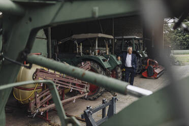 Älterer Geschäftsmann auf einem Bauernhof mit Traktor in einer Scheune - GUSF04039