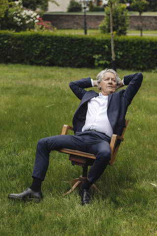 Entspannter älterer Geschäftsmann, der auf einem Stuhl in einem ländlichen Garten sitzt und nach oben schaut, lizenzfreies Stockfoto
