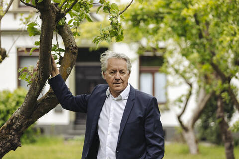 Porträt eines älteren Geschäftsmannes, der an einem Baum in einem ländlichen Garten steht, lizenzfreies Stockfoto