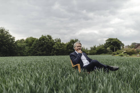 Senior businessman sitting on a chair in a field in the countryside - GUSF04069